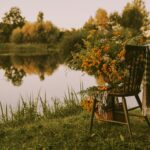 Empty chair sits beside a lake with flowers nearby, suggesting rest, reflection, and calm within a scenic environment.