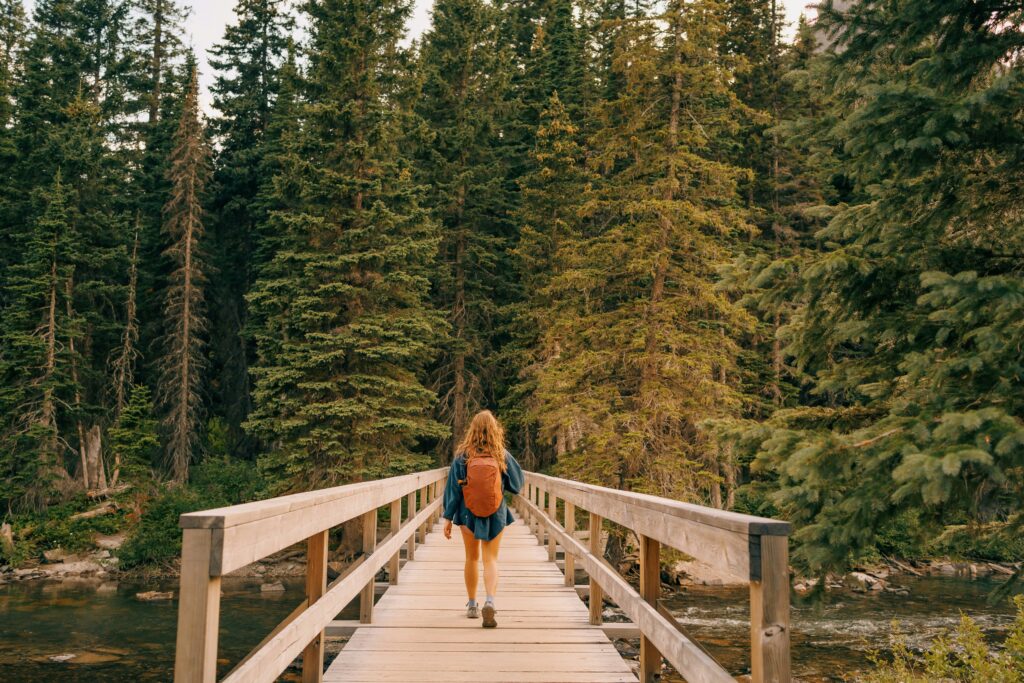 Woman walking across a forest bridge surrounded by trees, quiet scene suggesting transition and reflection