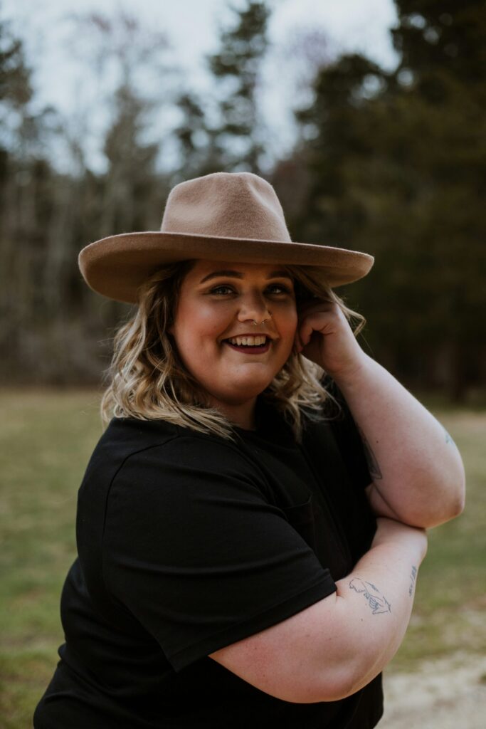 Woman smiling while wearing a hat outdoors, relaxed posture conveying warmth and ease