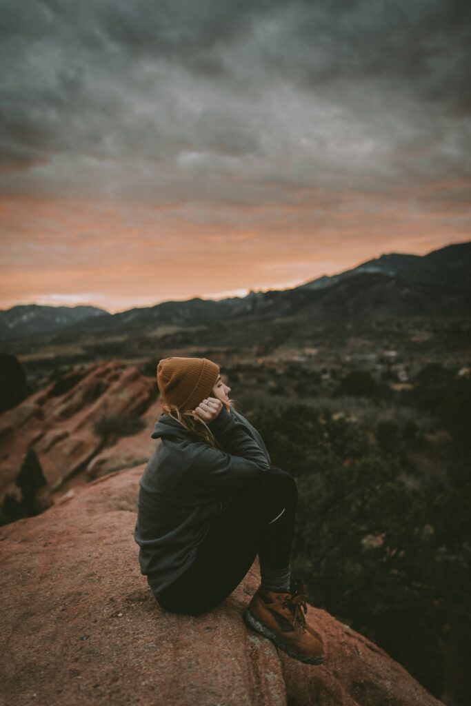 Woman stands on a mountaintop overlooking open land and sky, capturing perspective and strength.