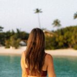 Woman viewed from behind, standing before a beach horizon, with a quiet posture suggesting reflection and stillness
