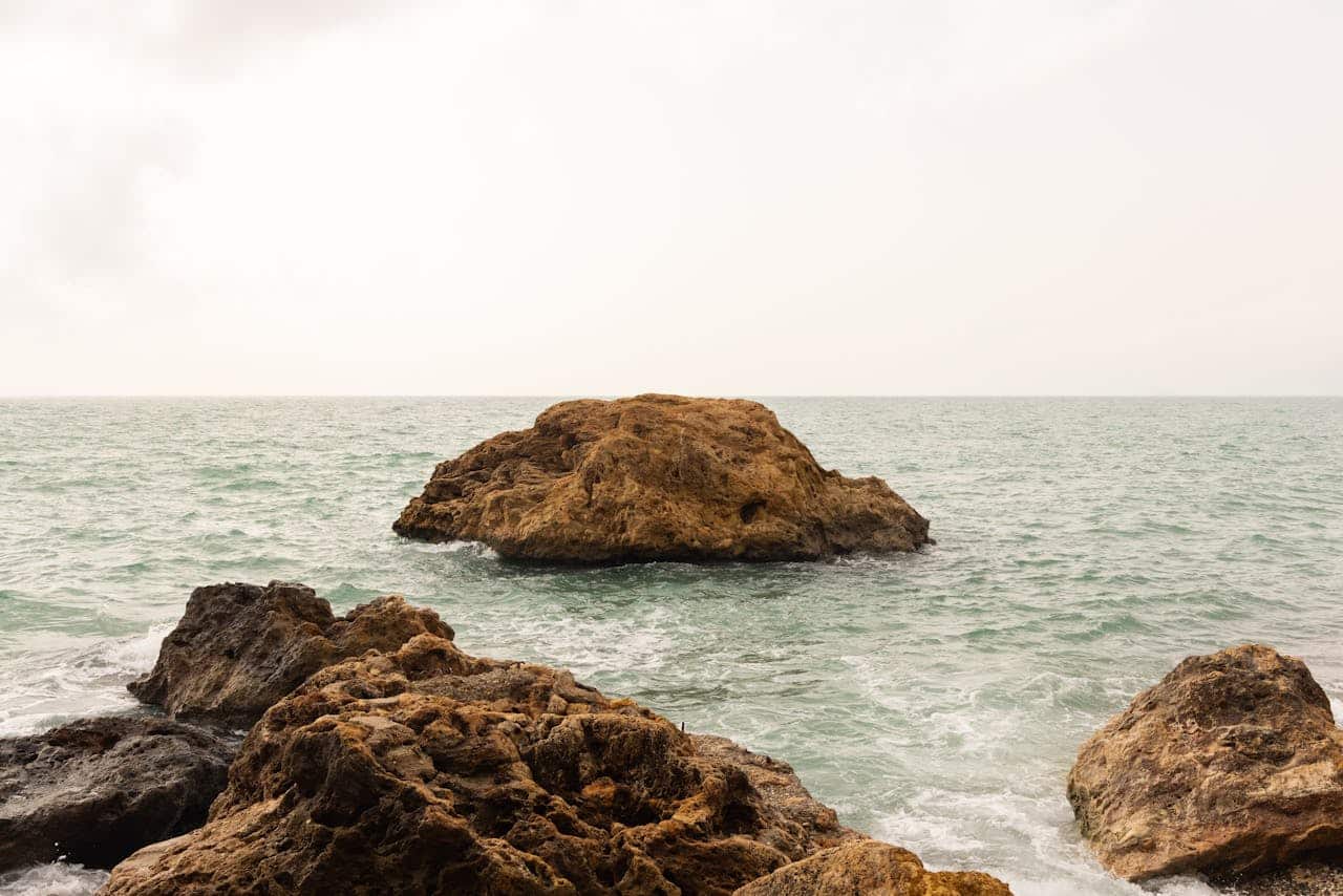rocky shoreline with large stone formation in calm ocean water