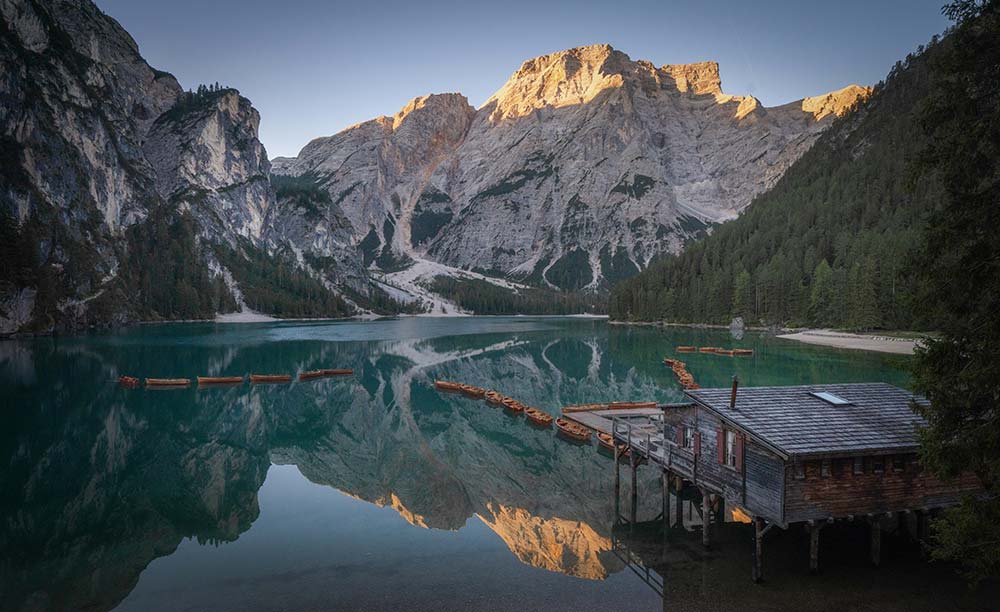  Mountain lake with a small cottage and boats surrounded by scenic peaks