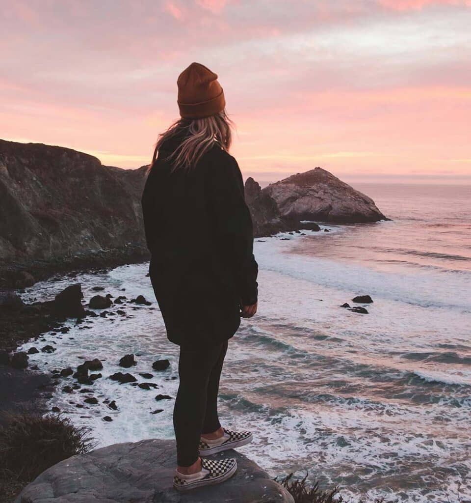 Woman standing before a beach at sunset, soft light surrounding her in a quiet, reflective moment