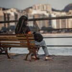 Woman sitting on a bridge overlooking flowing water, calm setting suggesting rest and contemplation