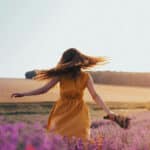  A woman walking through a lavender field, holding flowers and gently twirling in a peaceful, natural setting