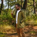  African American man holding a cup of coffee in a quiet forest, enjoying a slow, mindful moment in nature