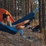  Woman resting in a hammock outdoors, smiling gently while surrounded by trees and natural light in a calm, relaxed setting