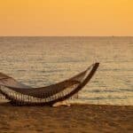 Empty hammock on a calm beach at sunset, soft waves and glowing sky creating a peaceful, restful atmosphere by the ocean.