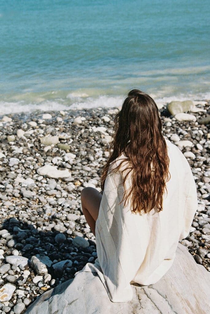  A woman sitting quietly on a rocky riverbank surrounded by small stones and calm flowing water
