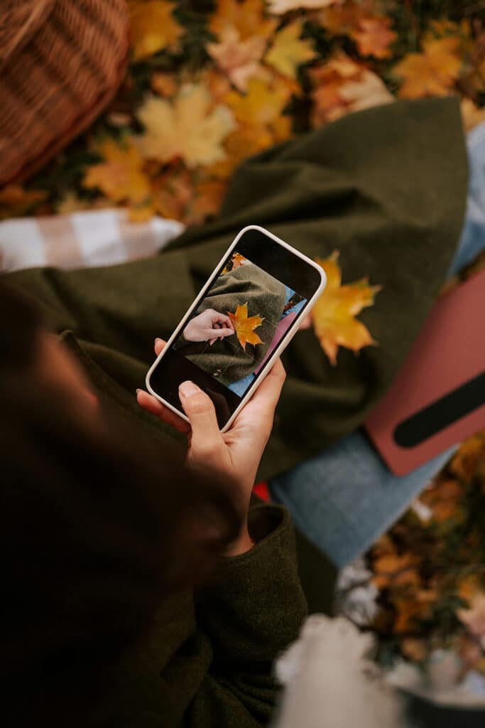  Hand holding a phone taking a close photo of a dried leaf outdoors during an autumn moment