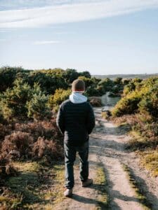  A man walking into nature, surrounded by greenery, evokes movement, solitude, and a sense of reflection.