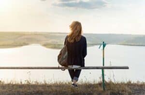  A woman sitting quietly on a bench facing a calm lake, creating a peaceful moment of reflection.