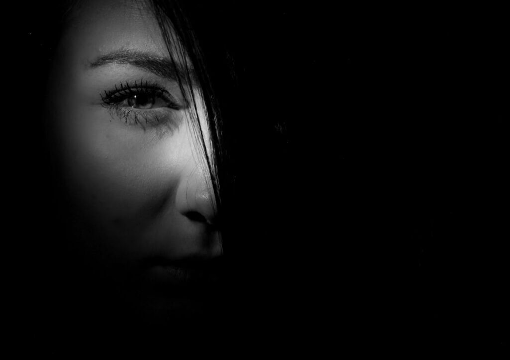 Close-up of a woman’s face half in shadow representing emotional trauma and inner psychological struggle addressed in trauma therapy