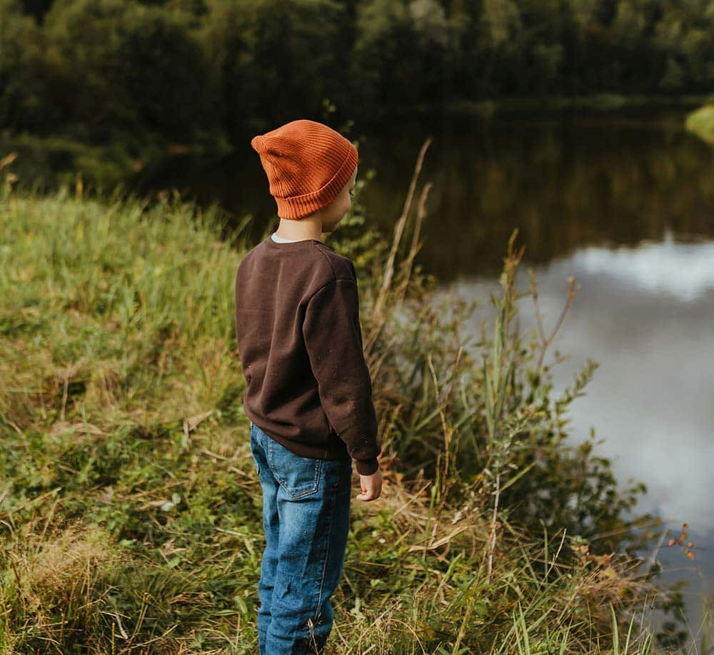  A young boy standing by the edge of a lake, reflecting quiet thought, emotional space, and inner awareness.