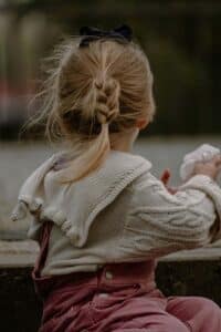  A young girl sitting outside holding a tissue, expressing vulnerability, sadness, and emotional processing.