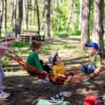  Children playing together in a hammock, one swinging while others sit, expressing joy, connection, and playfulness.