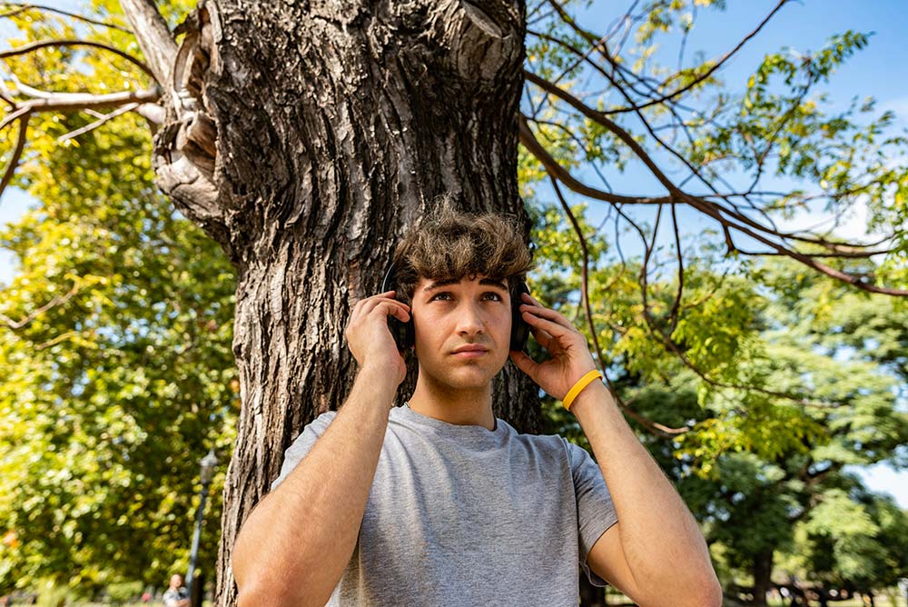 young man leaning on a tree while listening to music